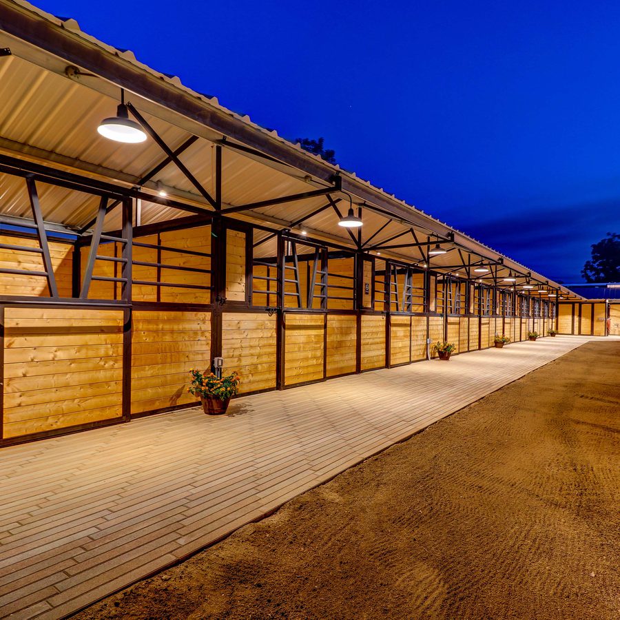 Barn aisle with stalls lit at dusk on a horse property marketed by Sharon Kaak