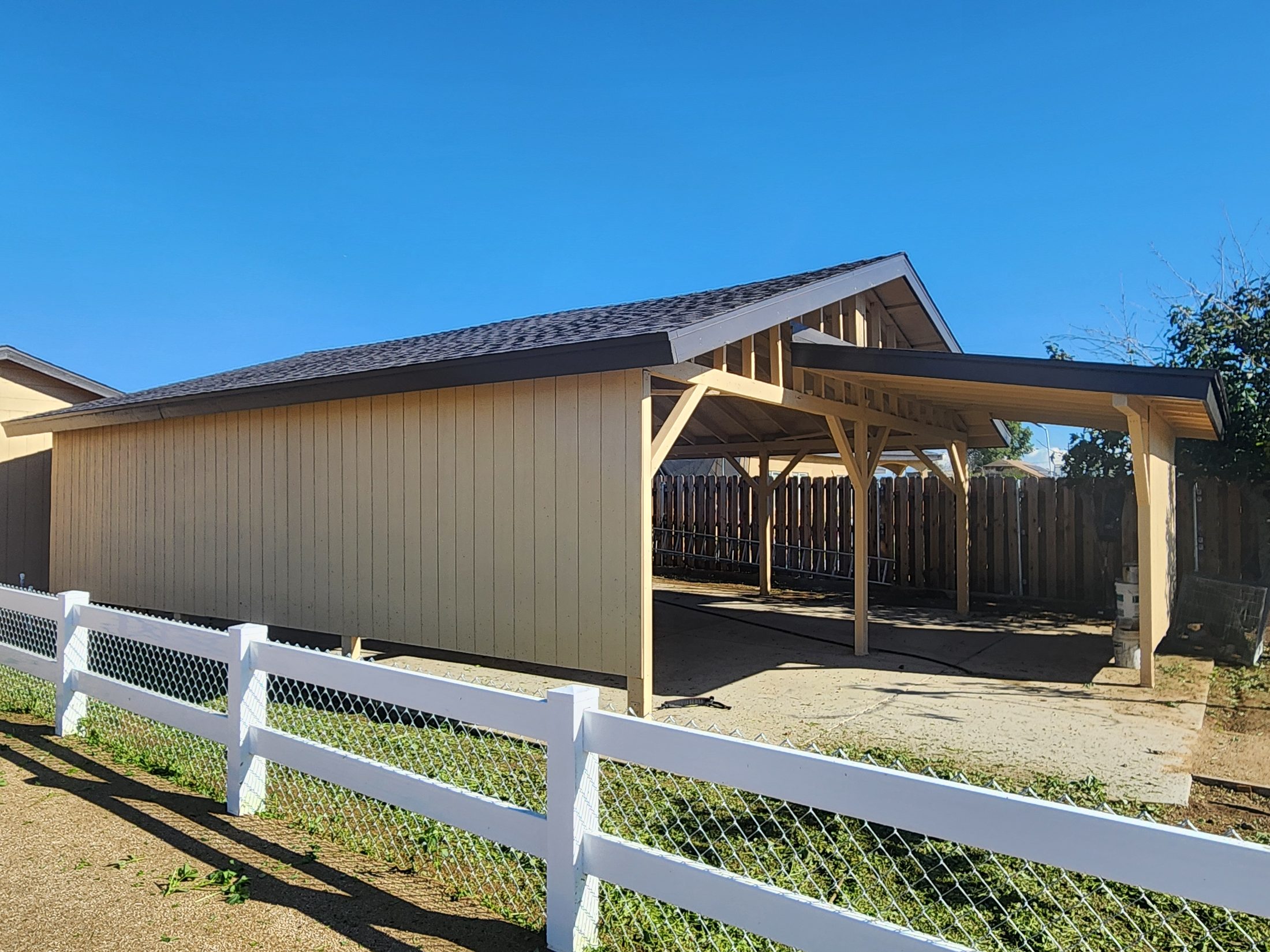 Barn and covered structure behind white fencing on a horse property