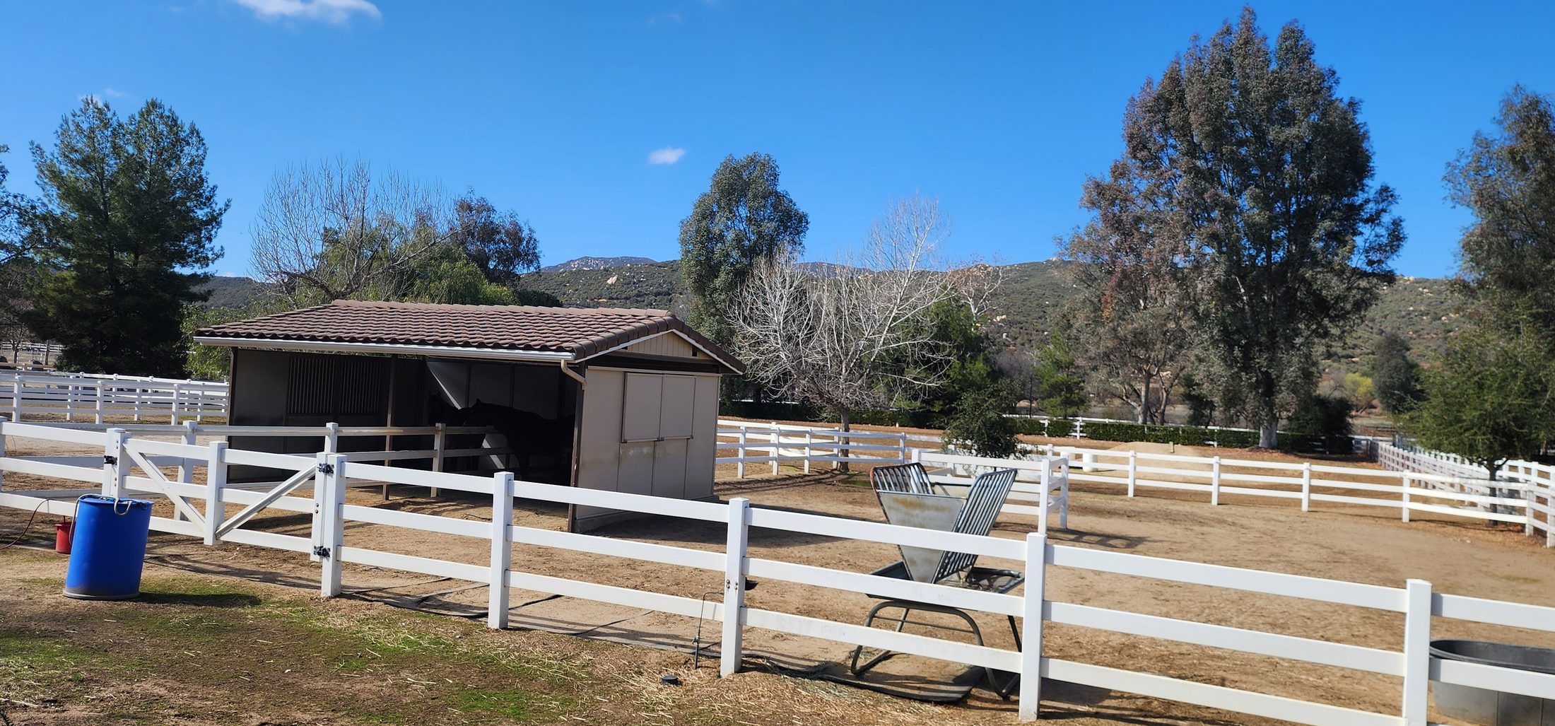 White-fenced paddock and shelter on an equestrian property with hills behind